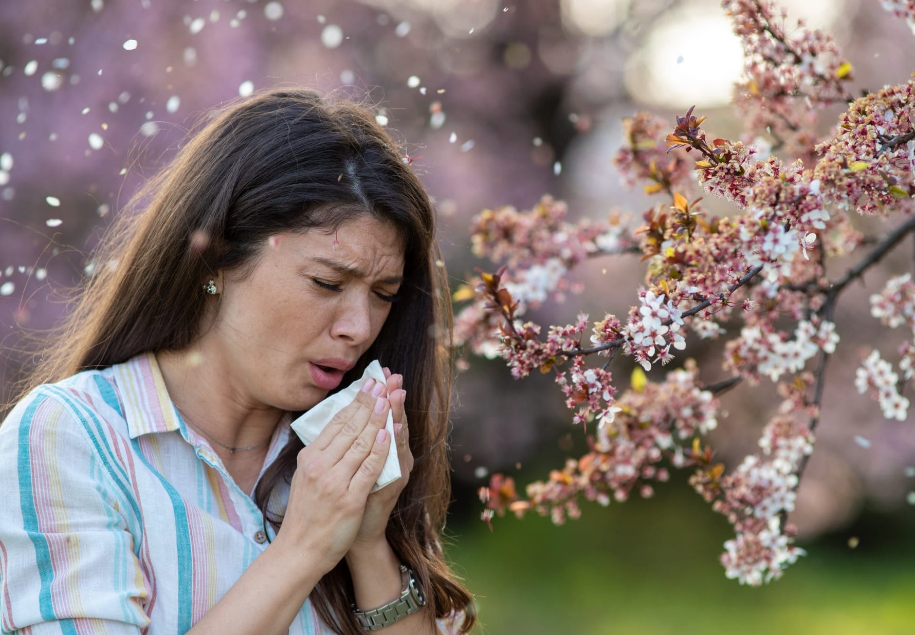 Donna con allergia stagionale ai pollini durante la fioritura primaverile, sintomi tipici delle allergie