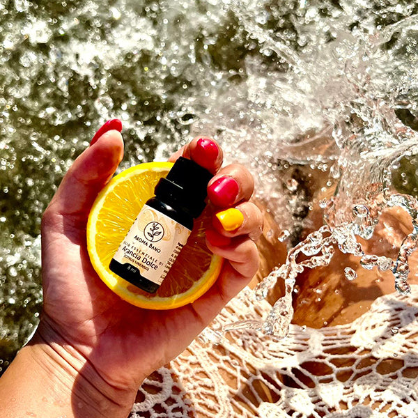 Olio essenziale di Arancia Dolce Aroma Bano tenuto in mano all’aperto con fetta di arancia